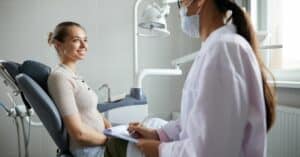 Side view portrait of pretty young woman sitting in dental chair and smiling at doctor during consultation in clinic