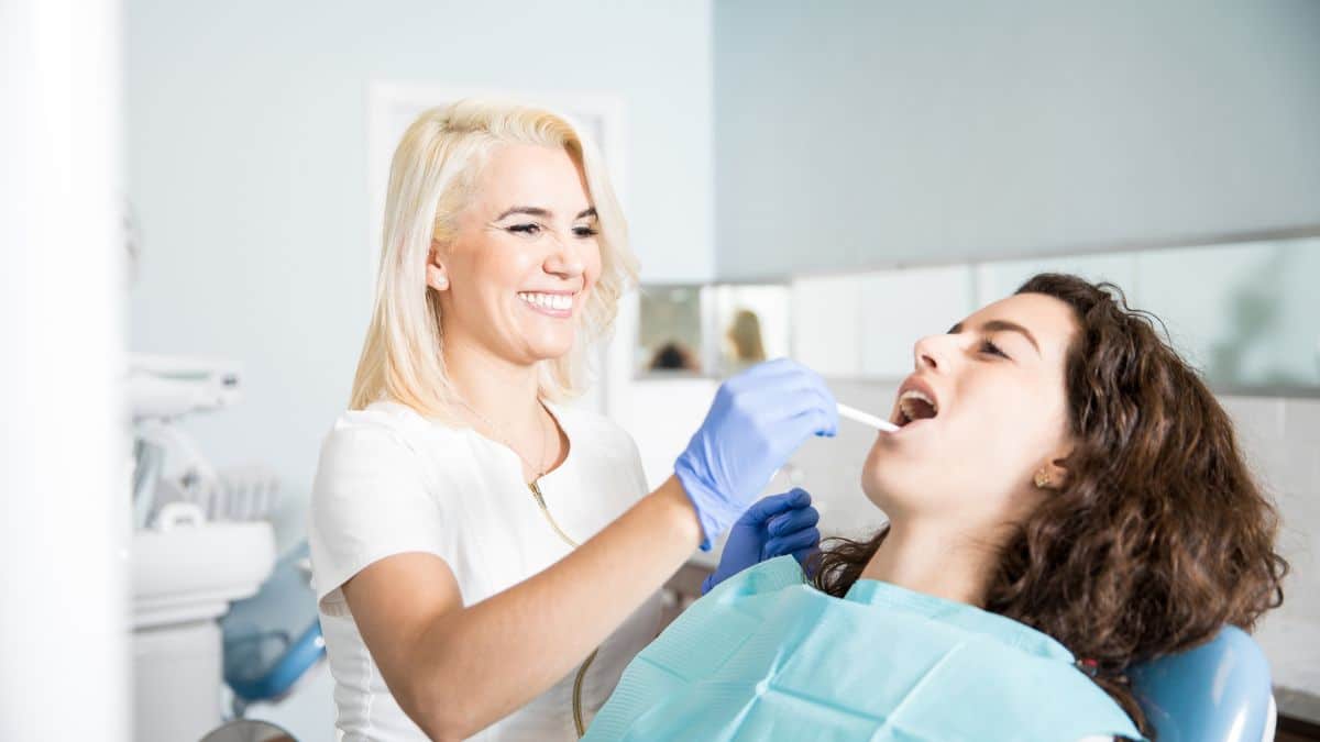 Happy female dentist doing checkup and cleaning patient mouth in dental clinic