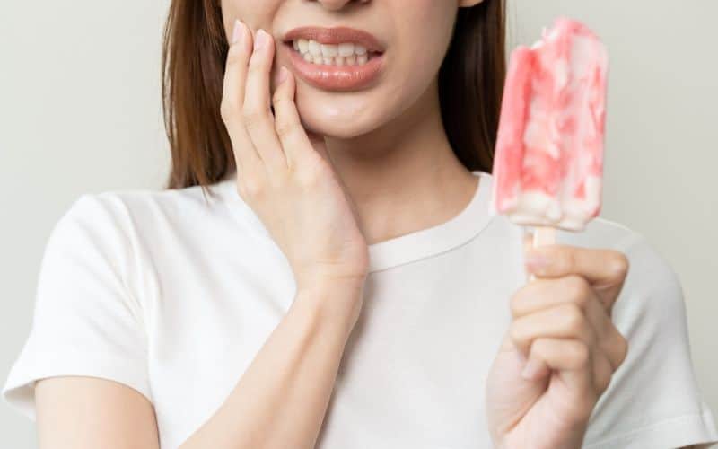 The woman experiences tooth sensitivity triggered by ice cream