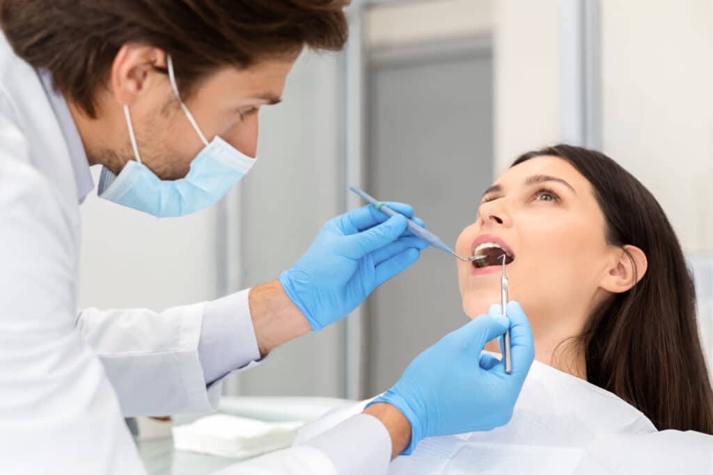 Young woman making check up in modern dental clinic, handsome doctor checking teeth