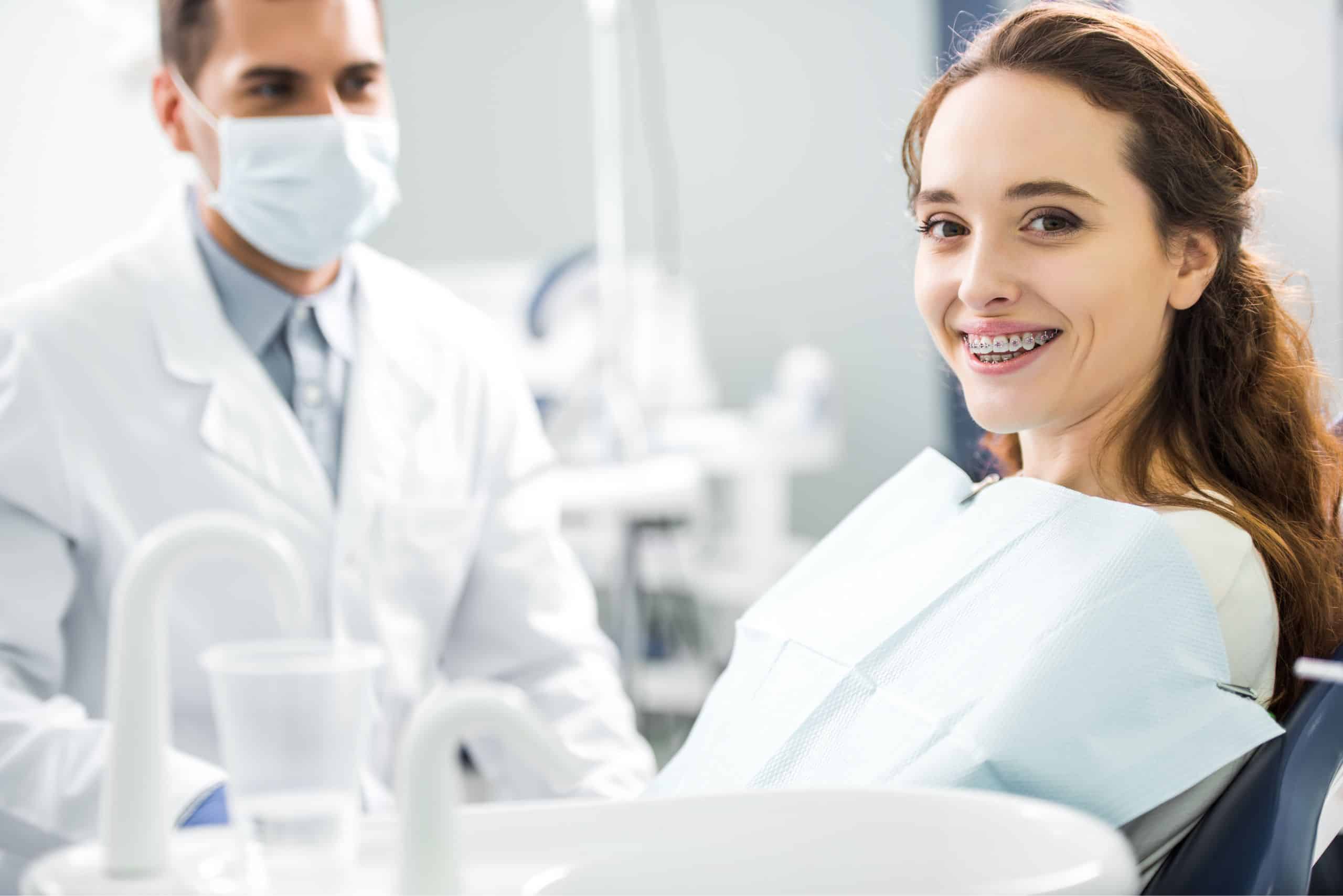 woman in braces smiling with orthodontist standing in mask