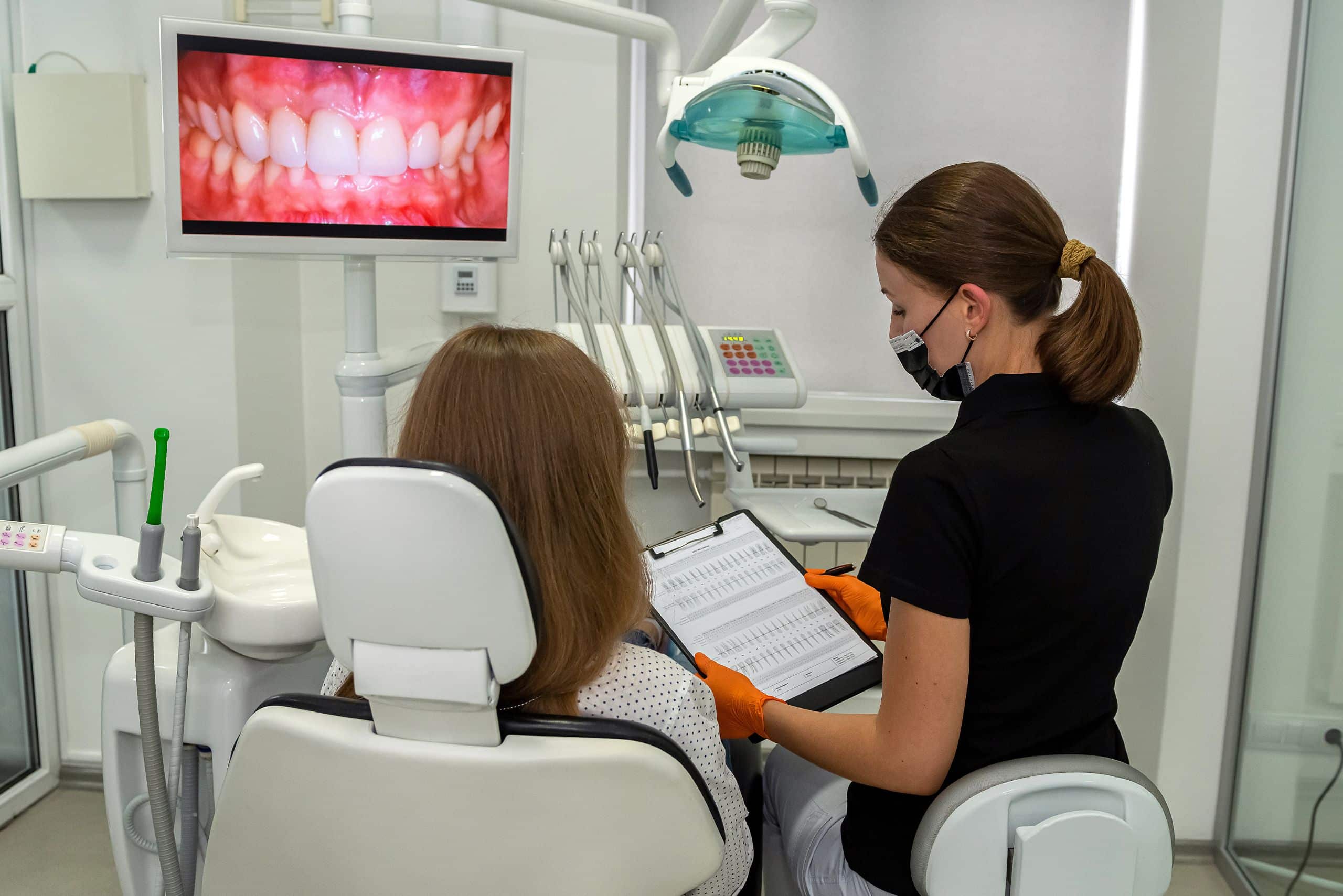Professional dentist with clipboard talking or recording diagnosis with patient before or after the treatment