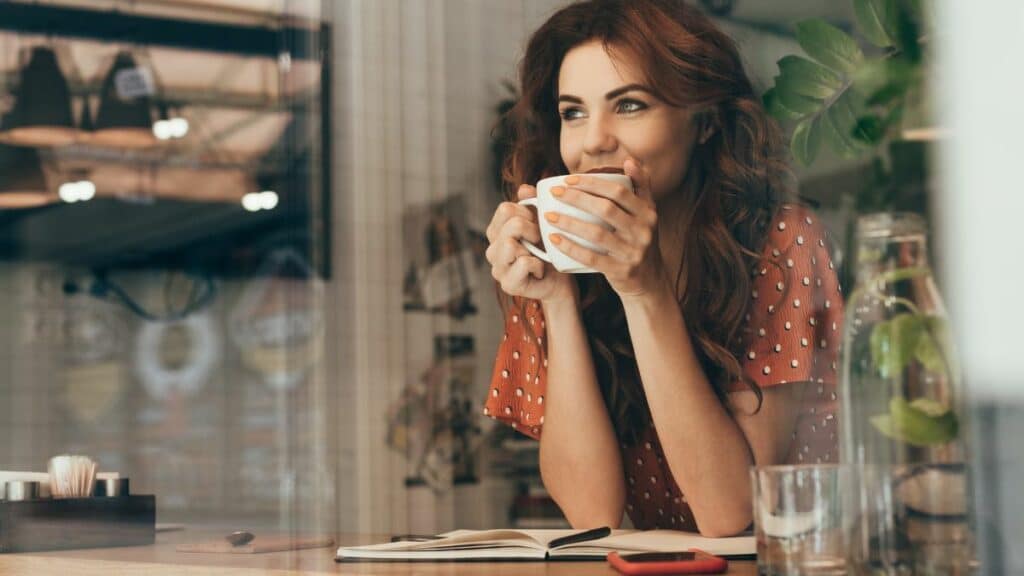 young woman drinking coffee at table with notebook