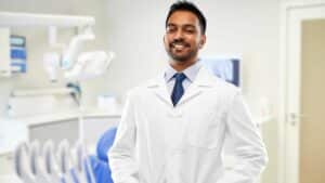 smiling indian male dentist in white coat over dental clinic