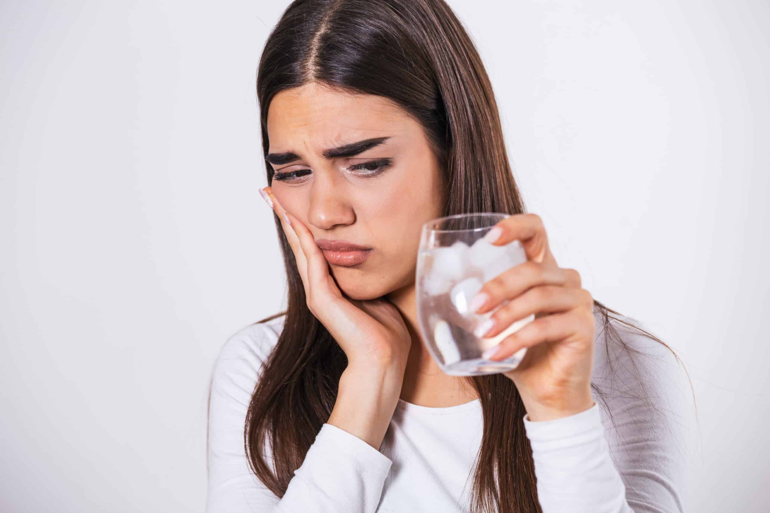 Young woman with sensitive teeth and hand holding glass of cold water with ice