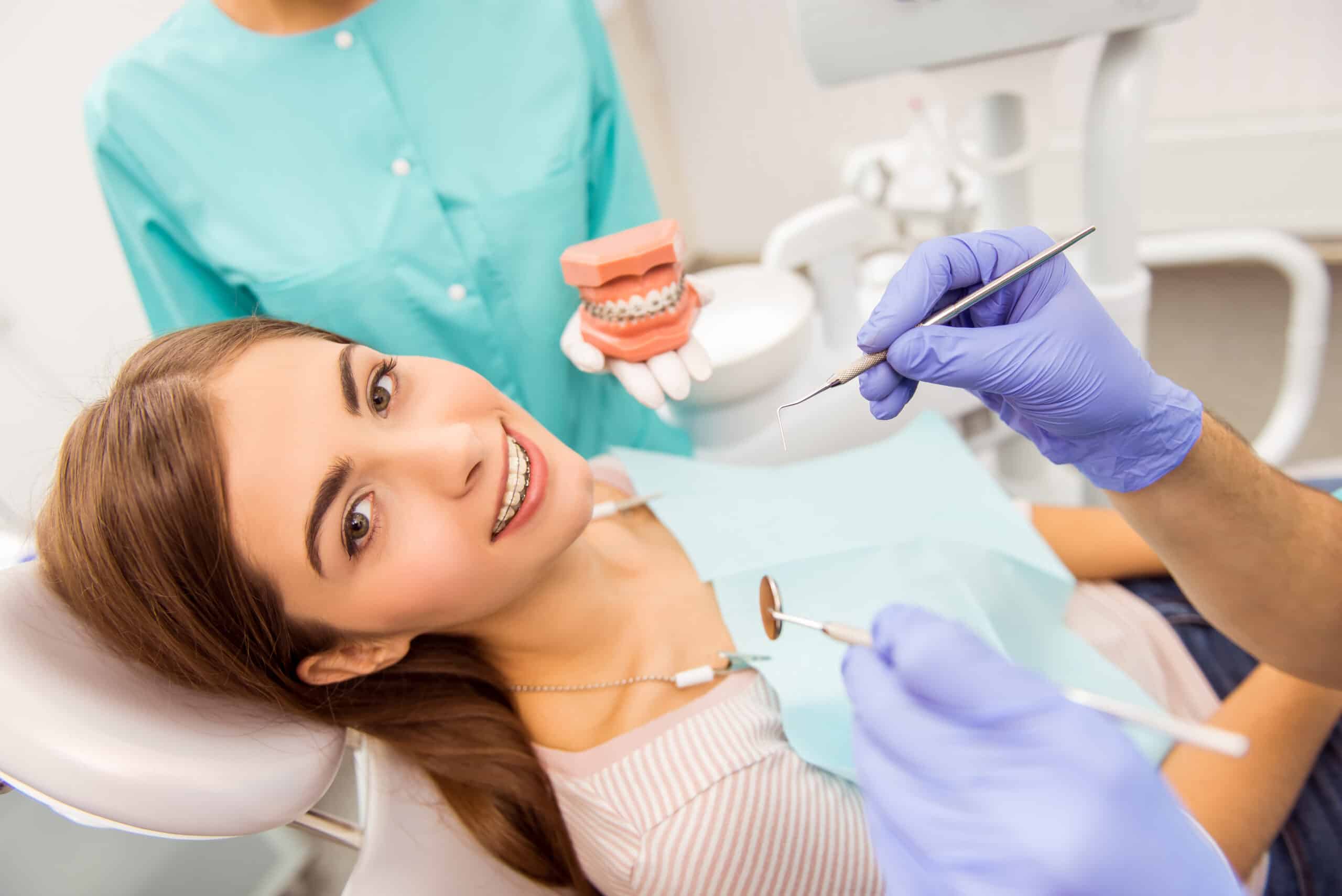 Attractive patient, with braces, treatment in dental, assistant to holding the model teeth