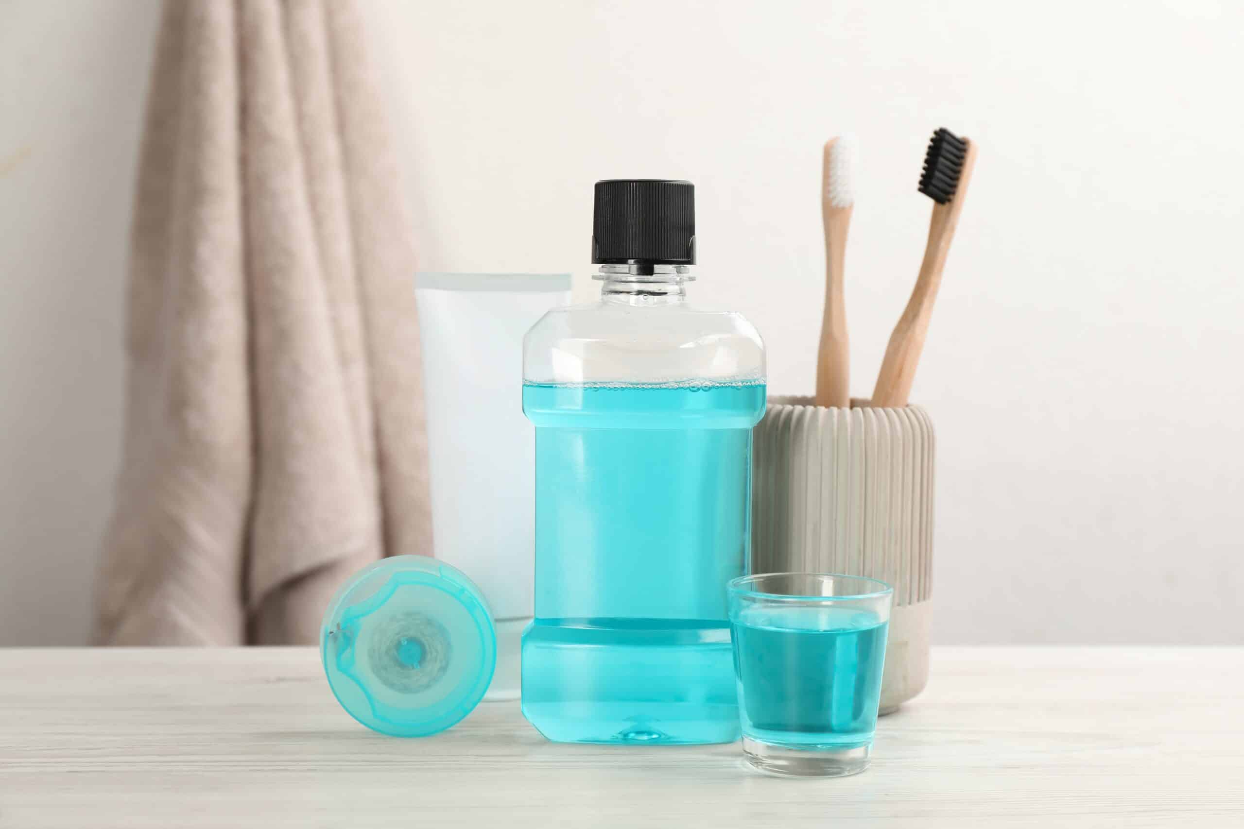 Mouthwash and other oral hygiene products on white wooden table in bathroom