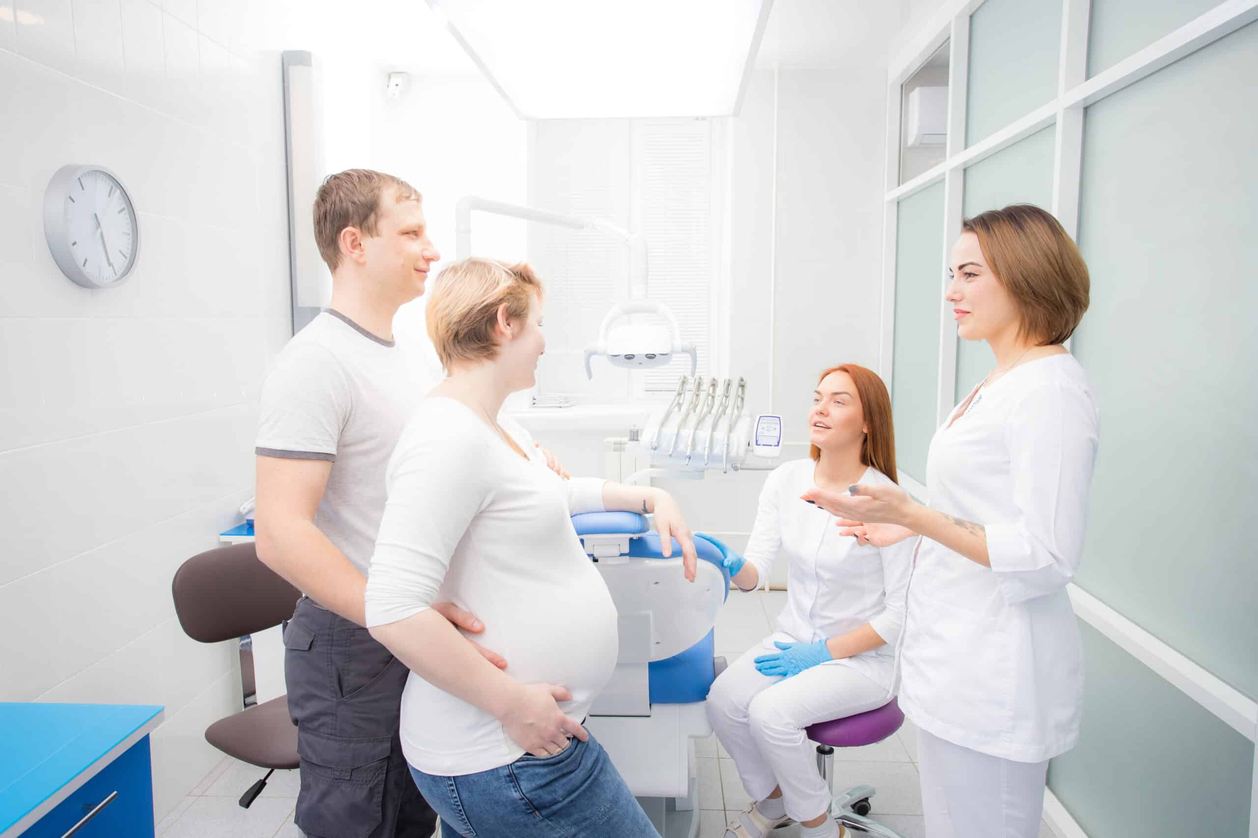 pregnant woman and her husband communicate with two young women dentists in a medical office